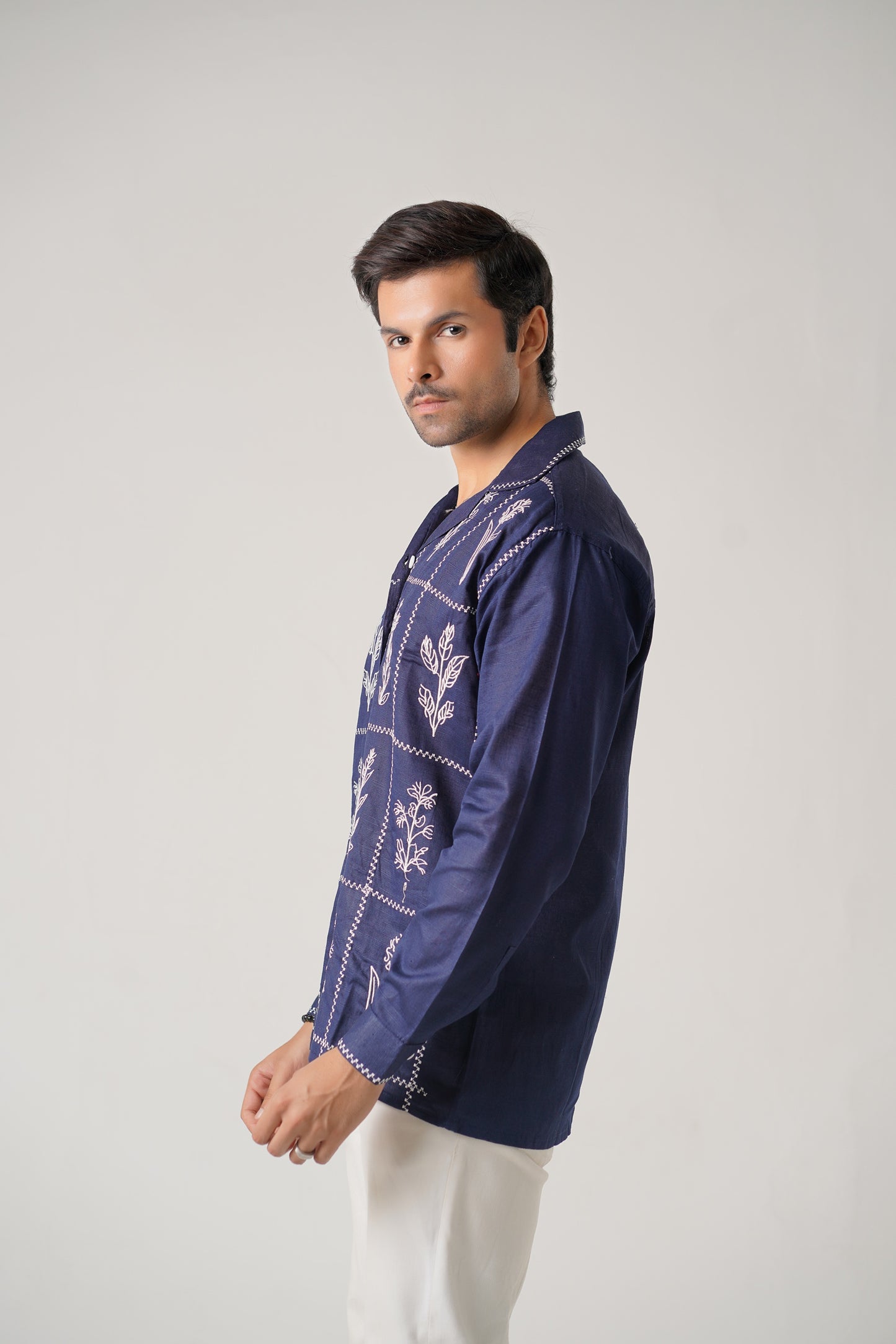 Man wearing a dark blue embroidered shirt on a light gray background