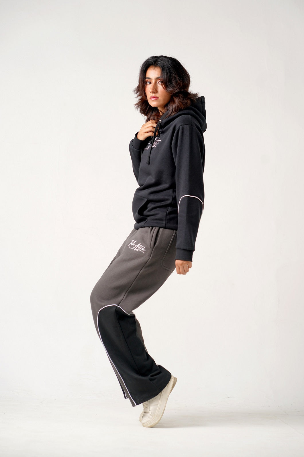 Person wearing a black hoodie and gray pants on a white background