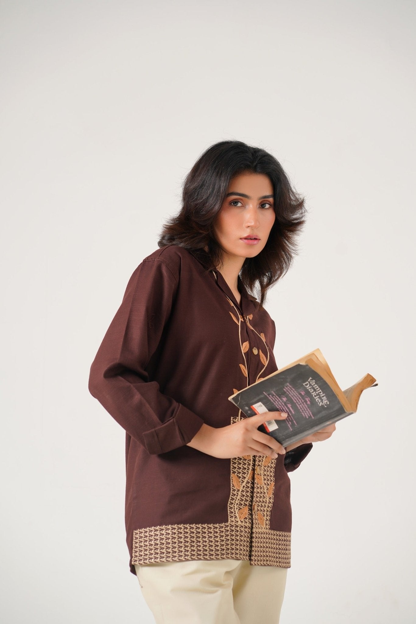 Woman wearing a brown traditional outfit holding a book on a white background