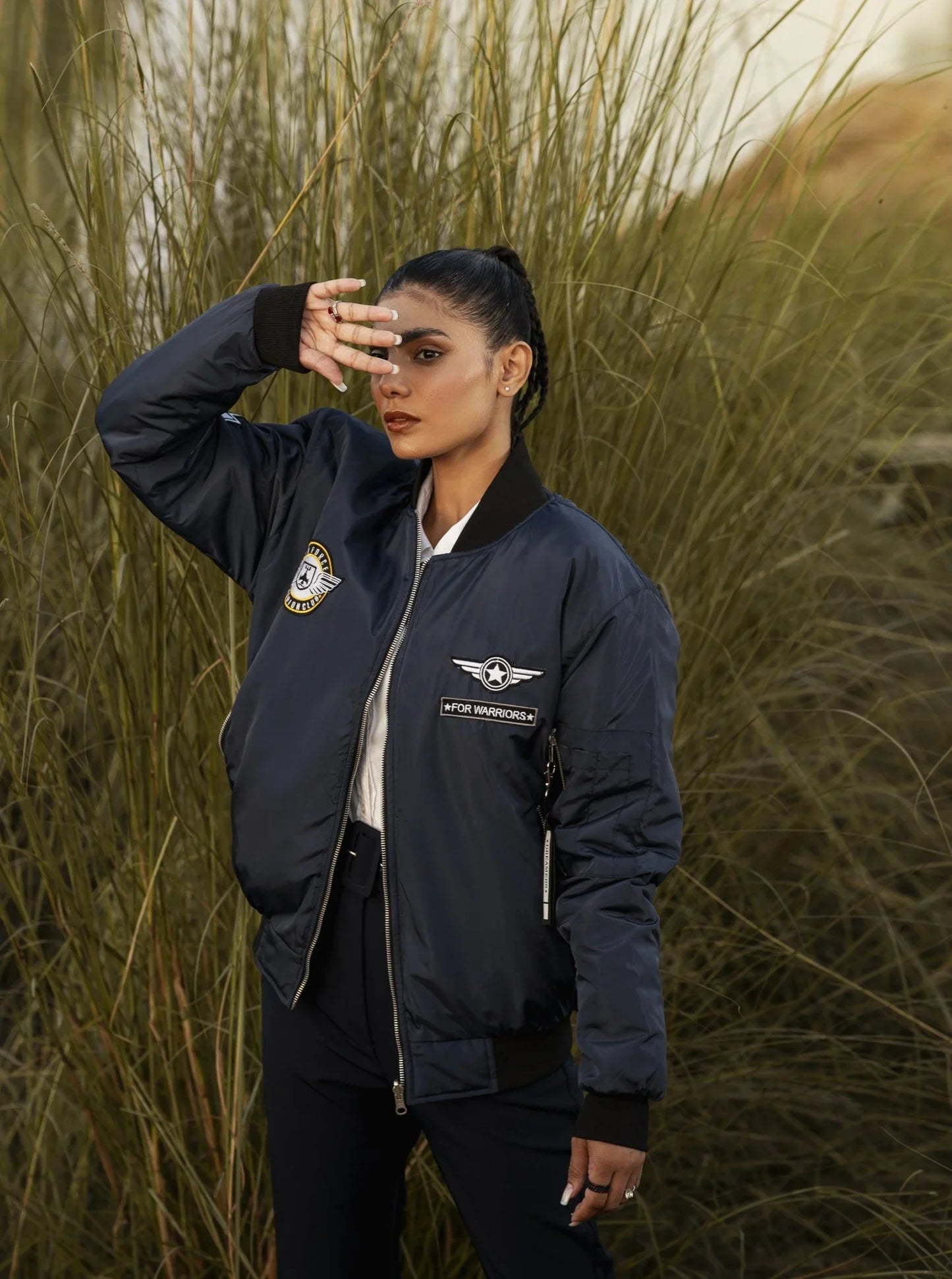 Person wearing a navy bomber jacket with logos in a natural setting