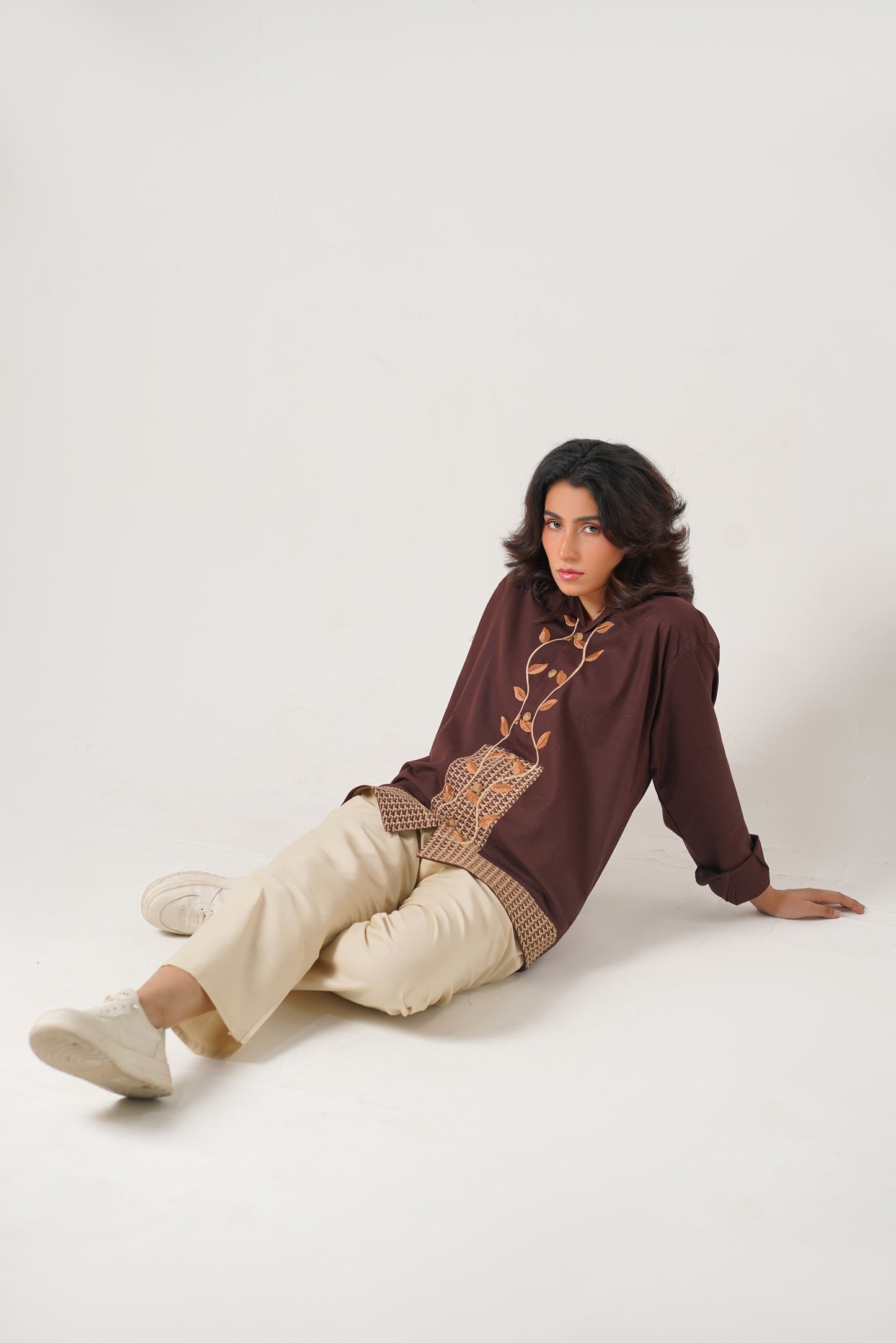 Woman wearing a brown sweater with intricate patterns sitting on a white background