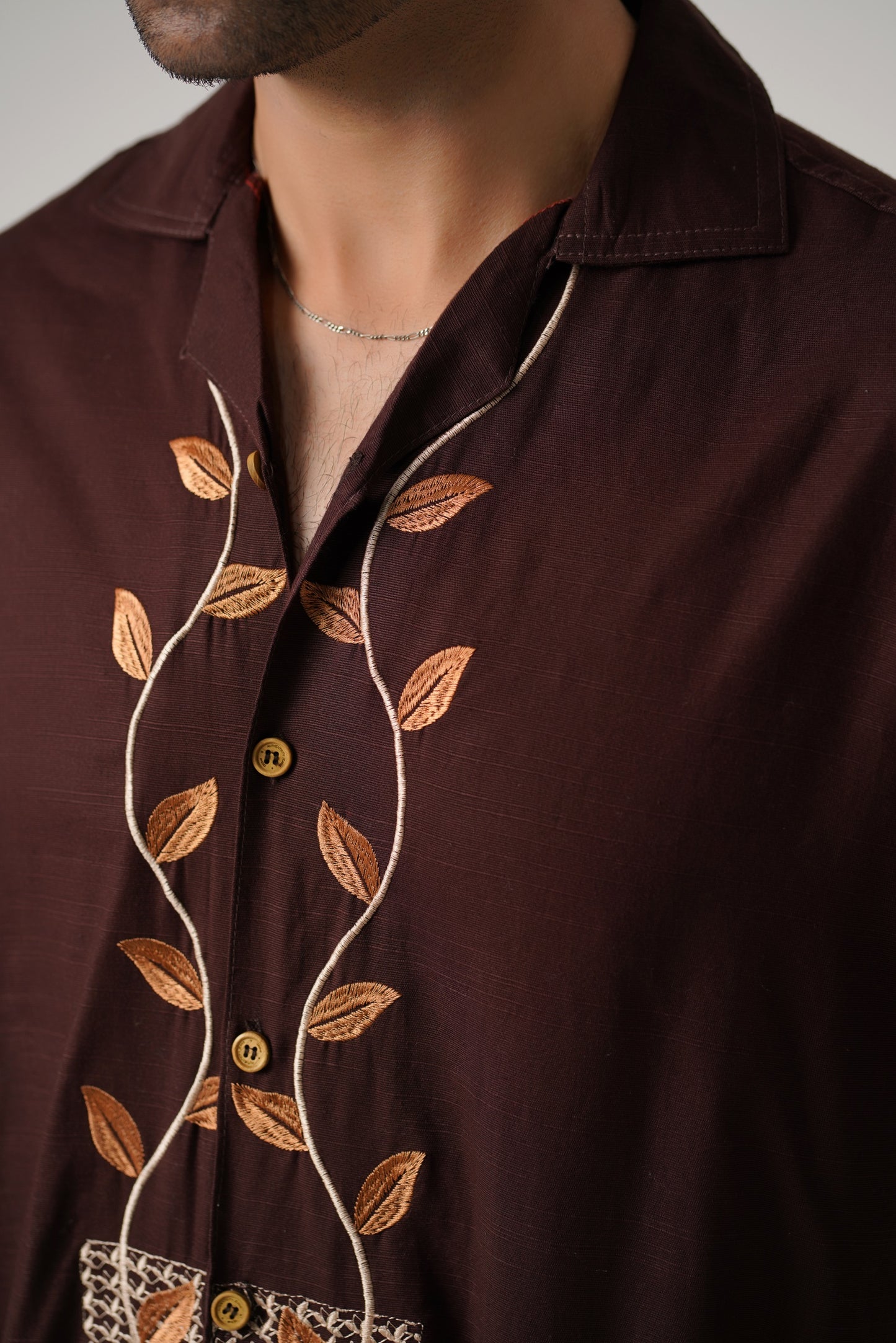 Brown shirt with leaf embroidery on a neutral background