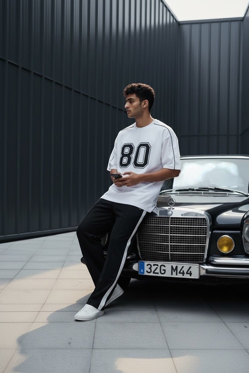 Koti Apparels white cotton blend t-shirt with black "80" graphic and piping. Model leans on a vintage car.
