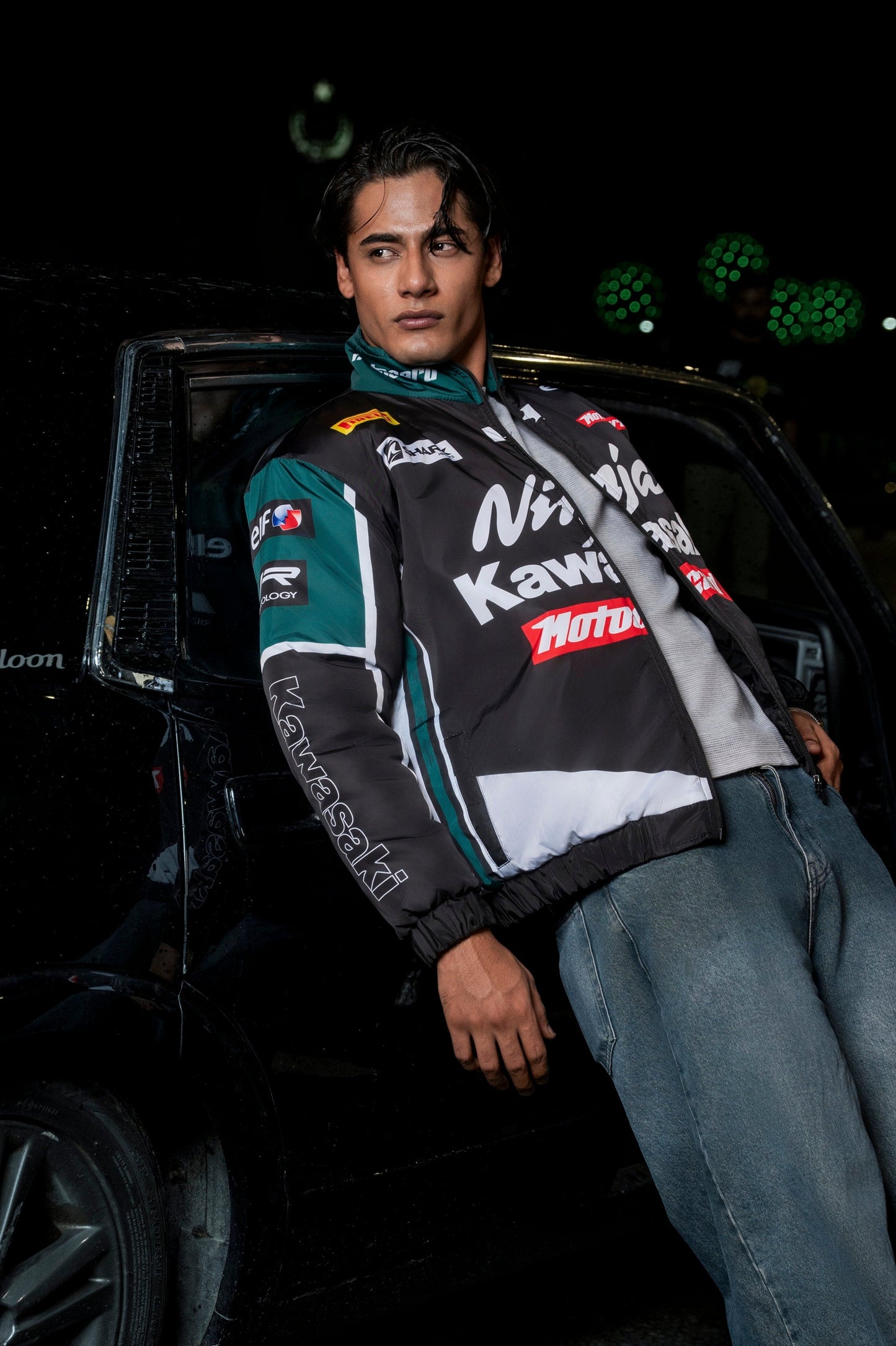 Koti Apparels Kawasaki racing jacket in black and green polyester worn by a man leaning against a car at night