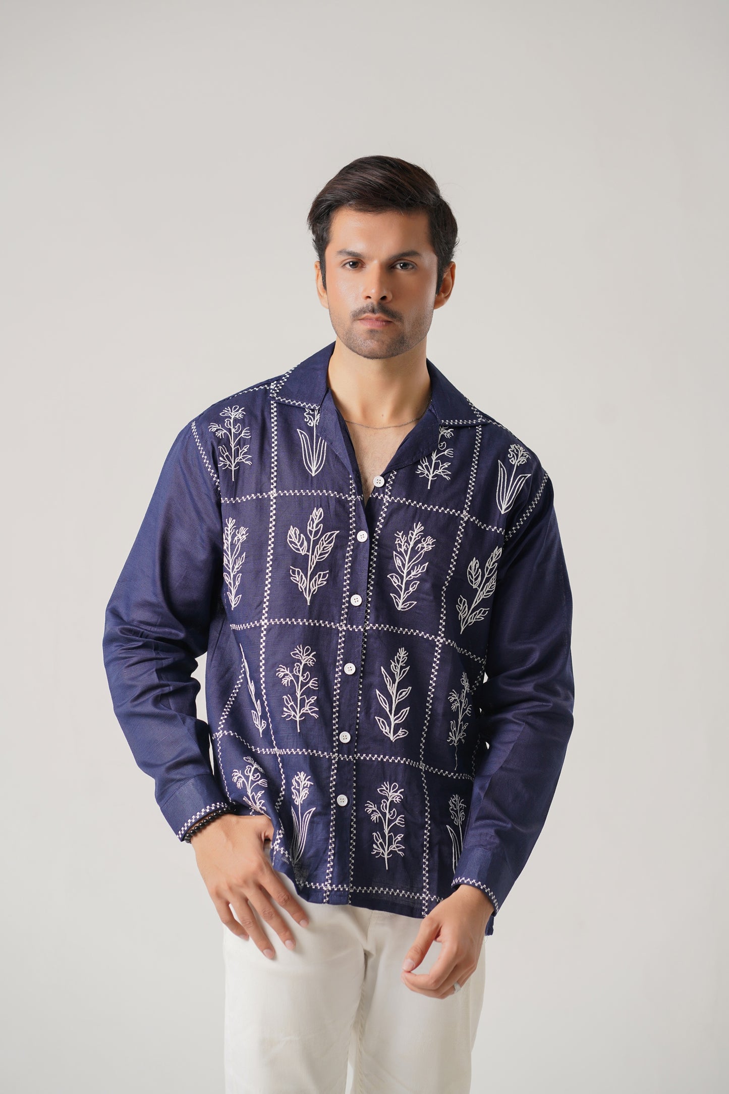 Man wearing a blue embroidered shirt with white patterns on a plain background