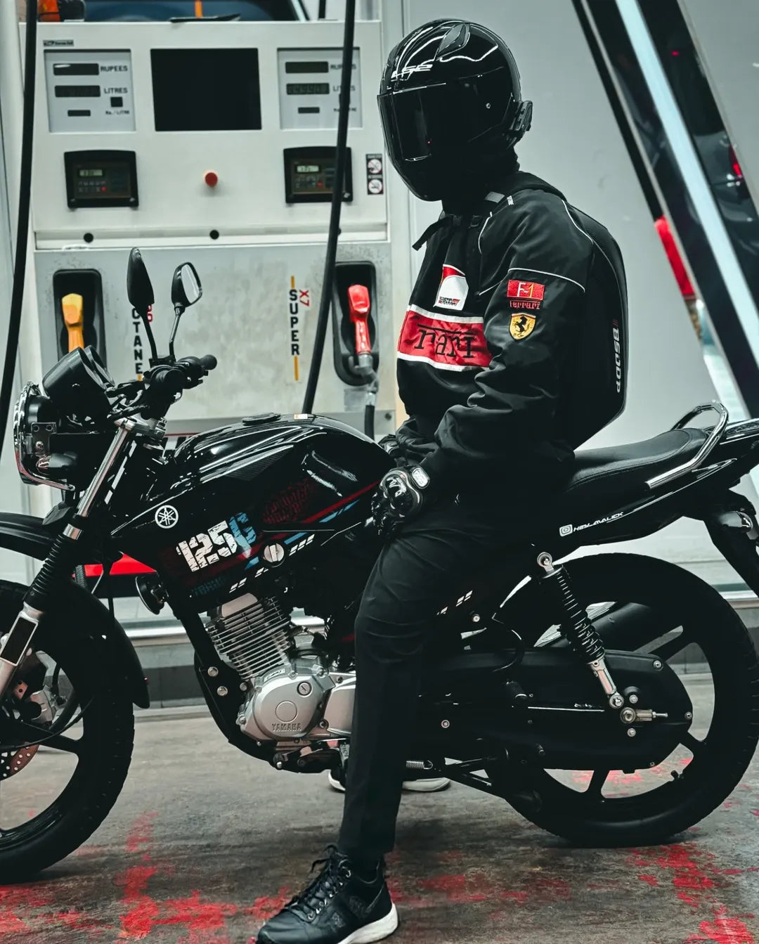 Person in a ferrari jacket and helmet sitting on a black motorcycle with a white vehicle in the background.