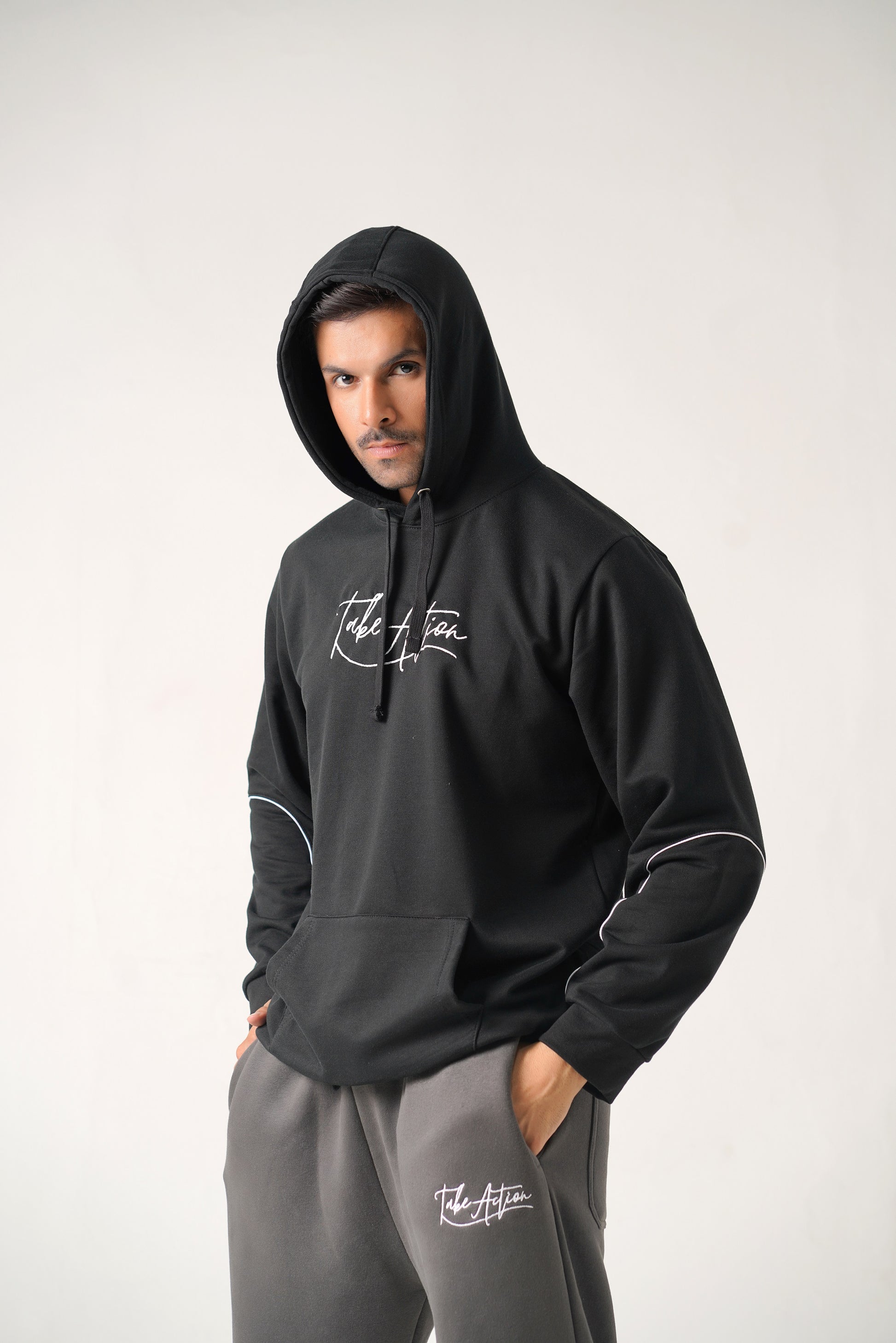 Person wearing a black hoodie and gray pants with branding on a white background