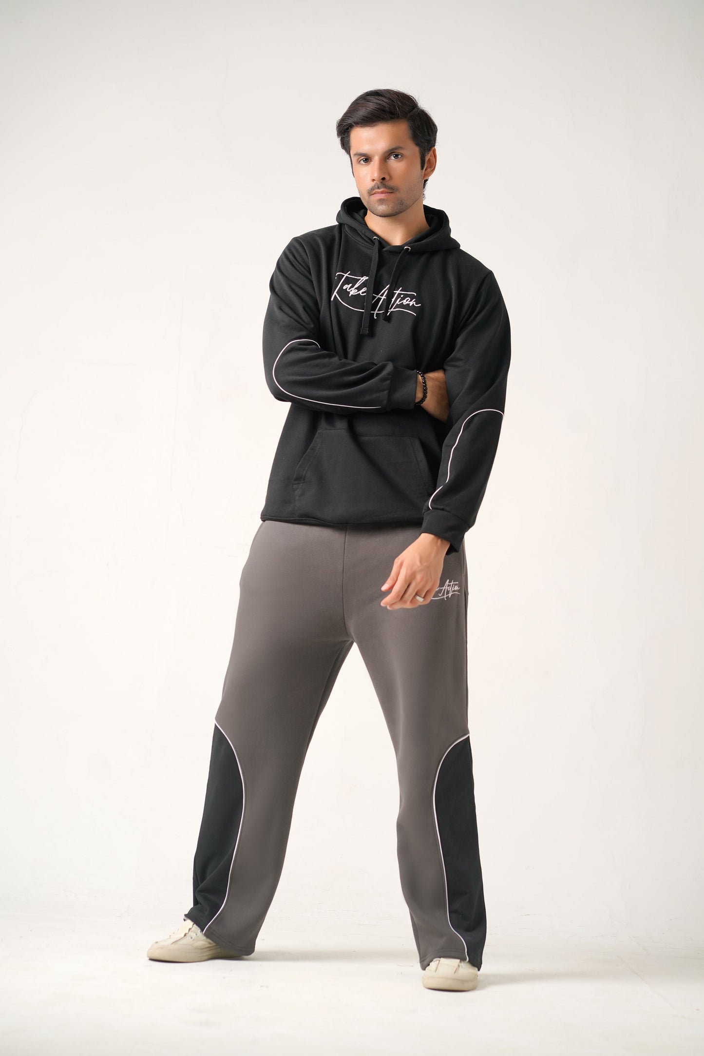 Man wearing a black hoodie and gray pants with branding on a white background