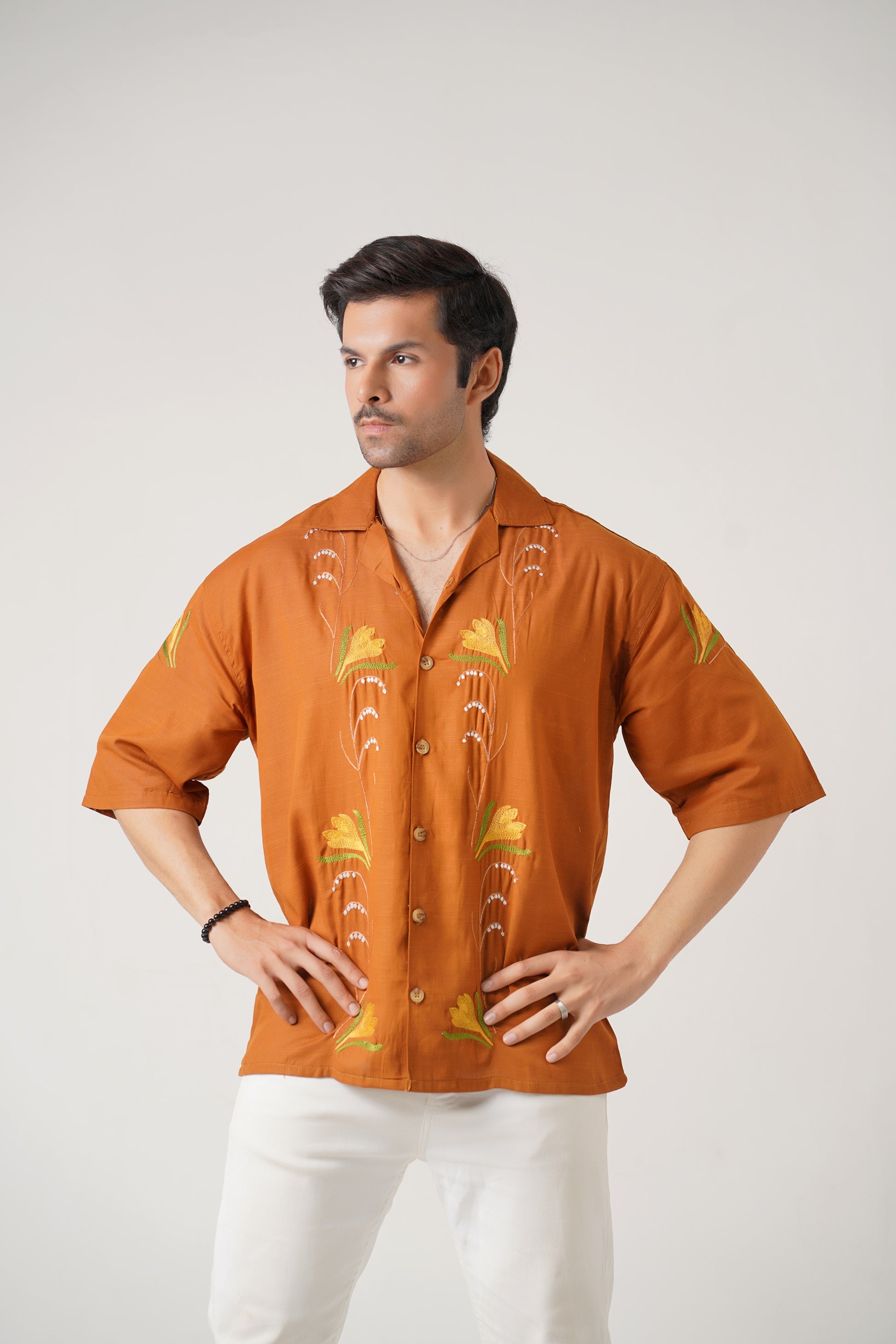 Man wearing an orange embroidered shirt with white pants on a light gray background