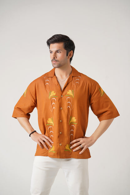 Man wearing an orange embroidered shirt with white pants on a light gray background