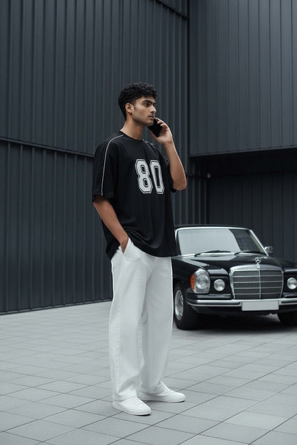 Koti Apparels black graphic baseball jersey t-shirt with white '80' graphic and piping on a man.