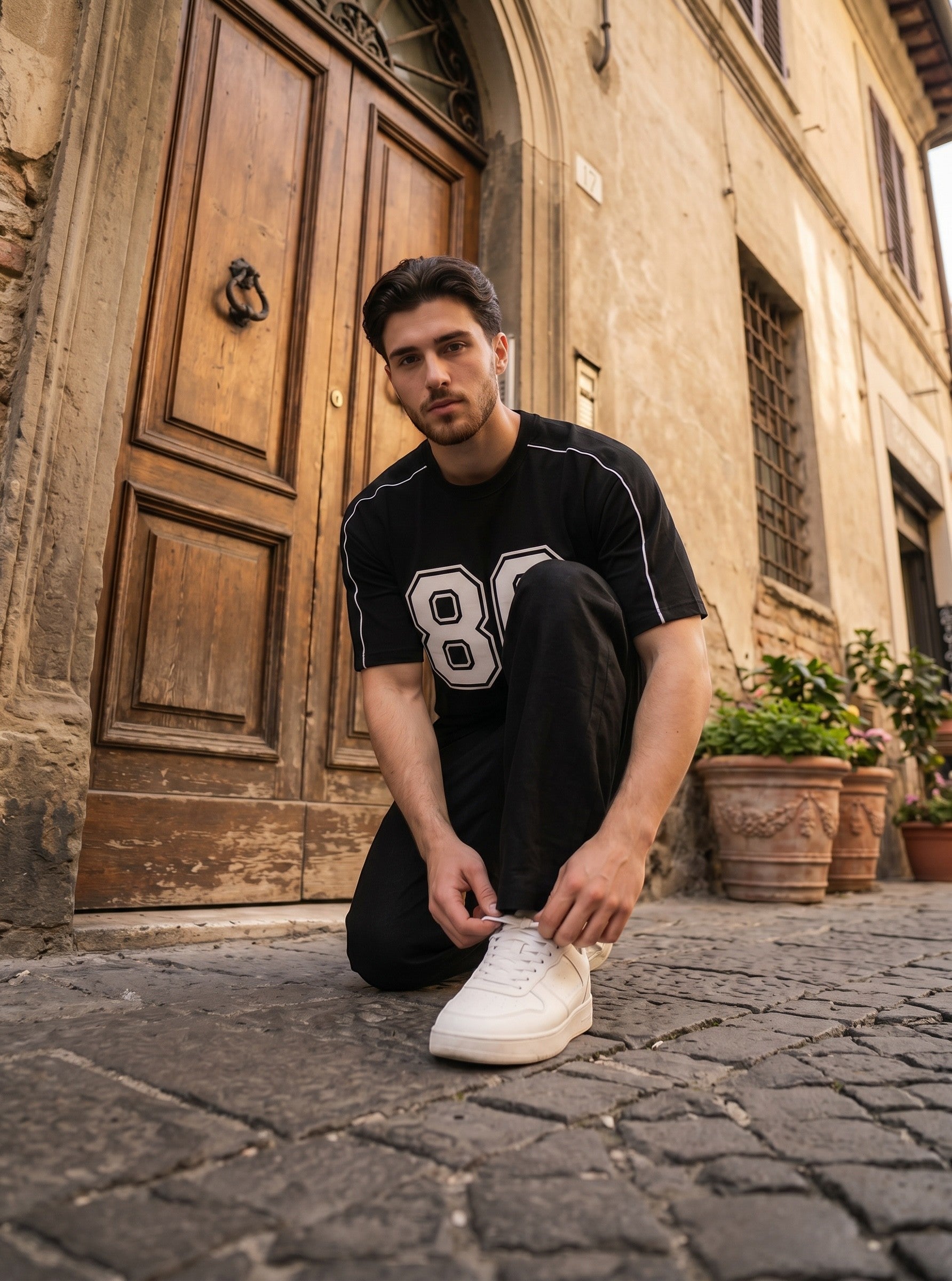 Koti Apparels black graphic baseball jersey with white 80 print and shoulder piping worn by a man on a cobblestone path