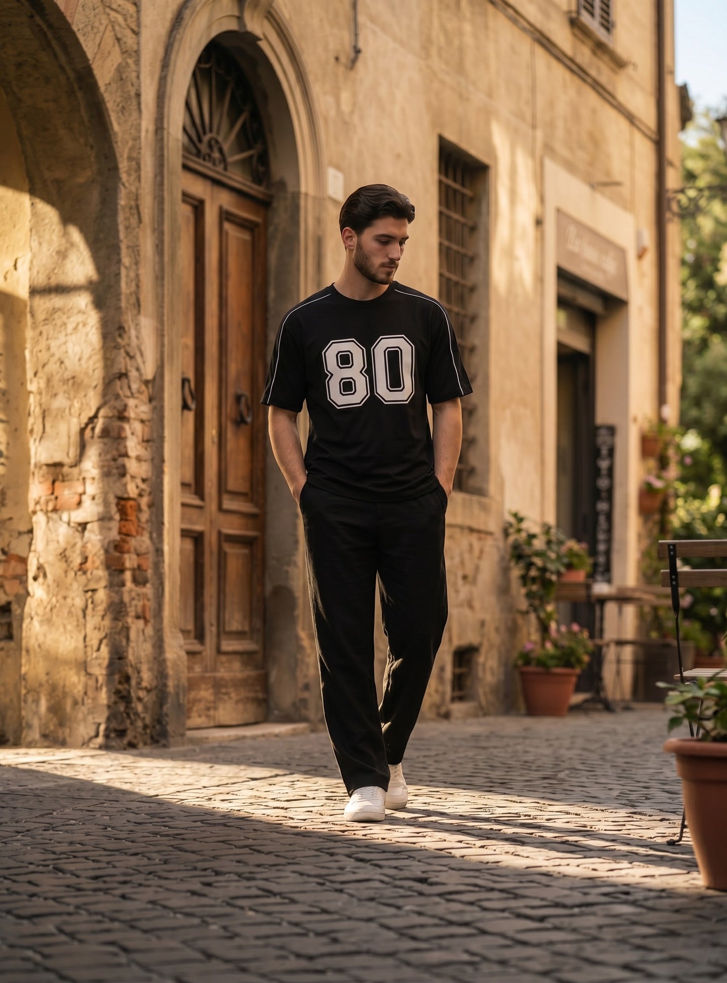 Koti Apparels black graphic baseball jersey with white 80 print and shoulder piping worn by a man on a cobblestone street
