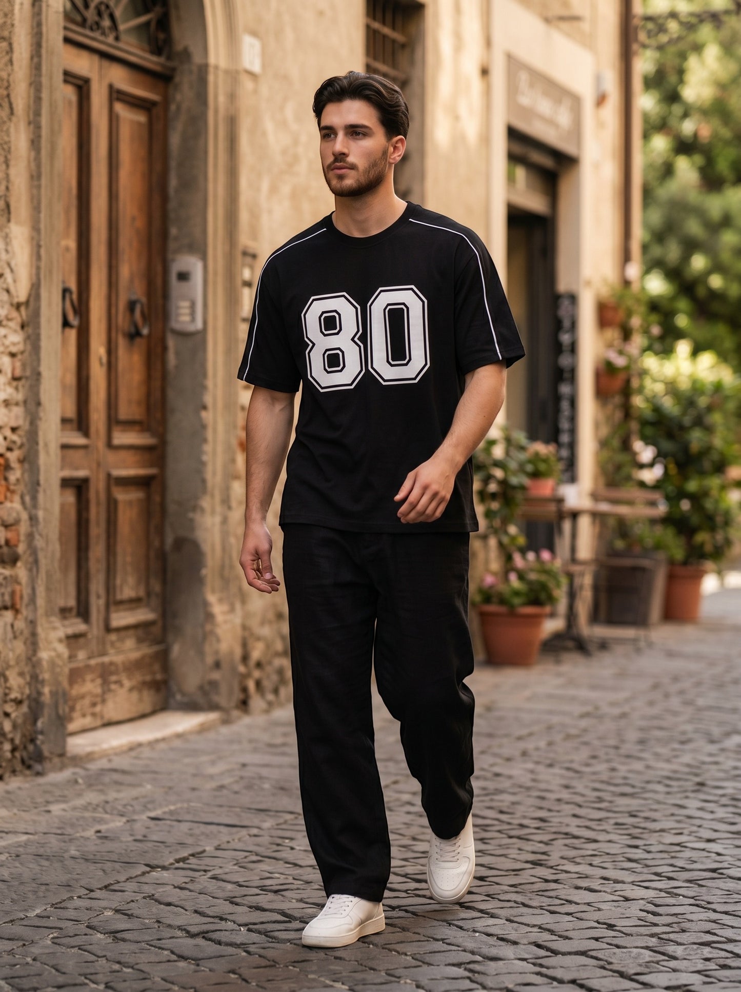 Koti Apparels black graphic baseball jersey with white 80 print and shoulder piping worn by a man on a city street.