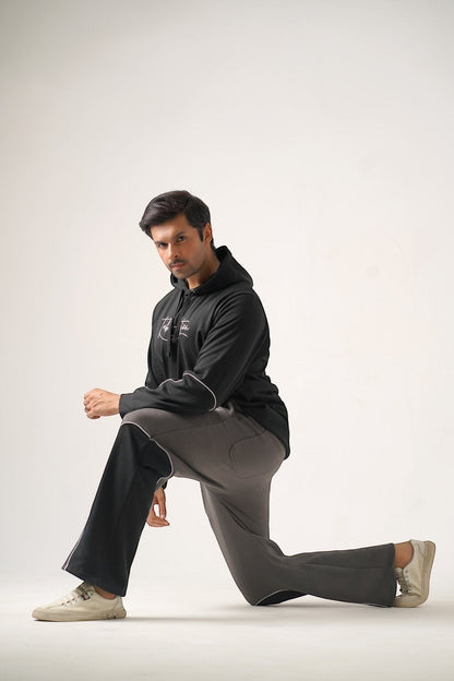 Koti Apparels black heavyweight cotton fleece hoodie with grey trousers, featuring embroidered logo and puff print graphic.