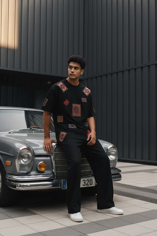 Koti Apparels black cotton t-shirt with colorful oriental rug patchwork details, relaxed fit, worn by a man sitting on a vintage car.