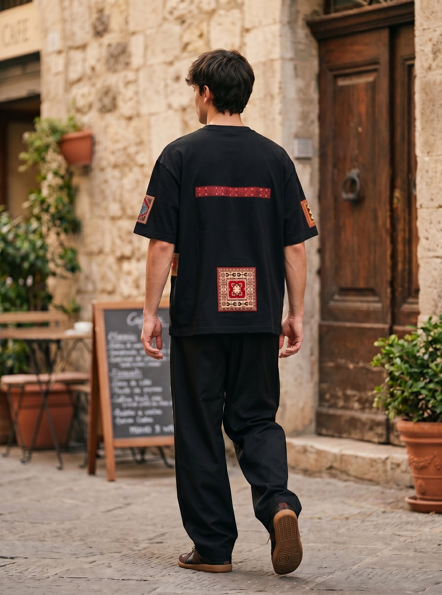 Koti Apparels black cotton t-shirt with vintage rug-inspired patchwork on the back, worn by a man on a stone street.
