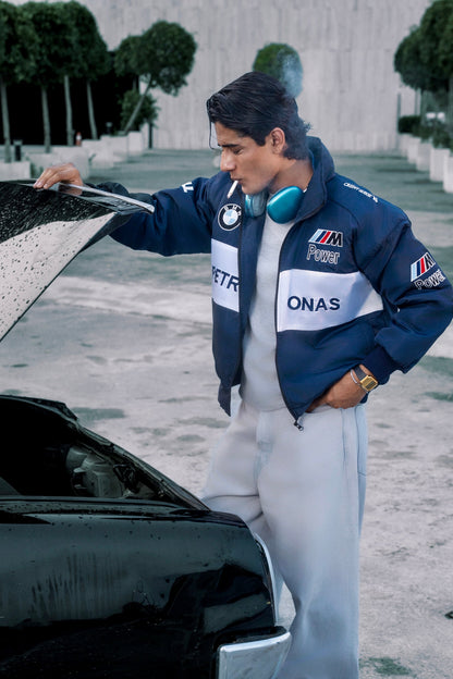 Koti Apparels BMW racing jacket with embroidered motorsport logos worn by a man looking under a car hood outdoors