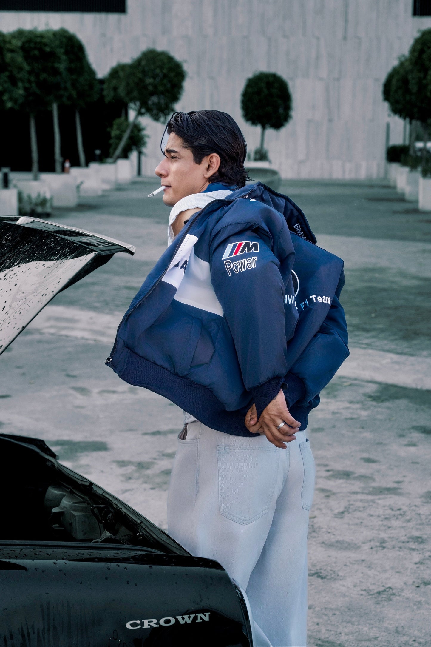 Koti Apparels navy blue BMW racing jacket with embroidered motorsport logos worn by a man standing by a car