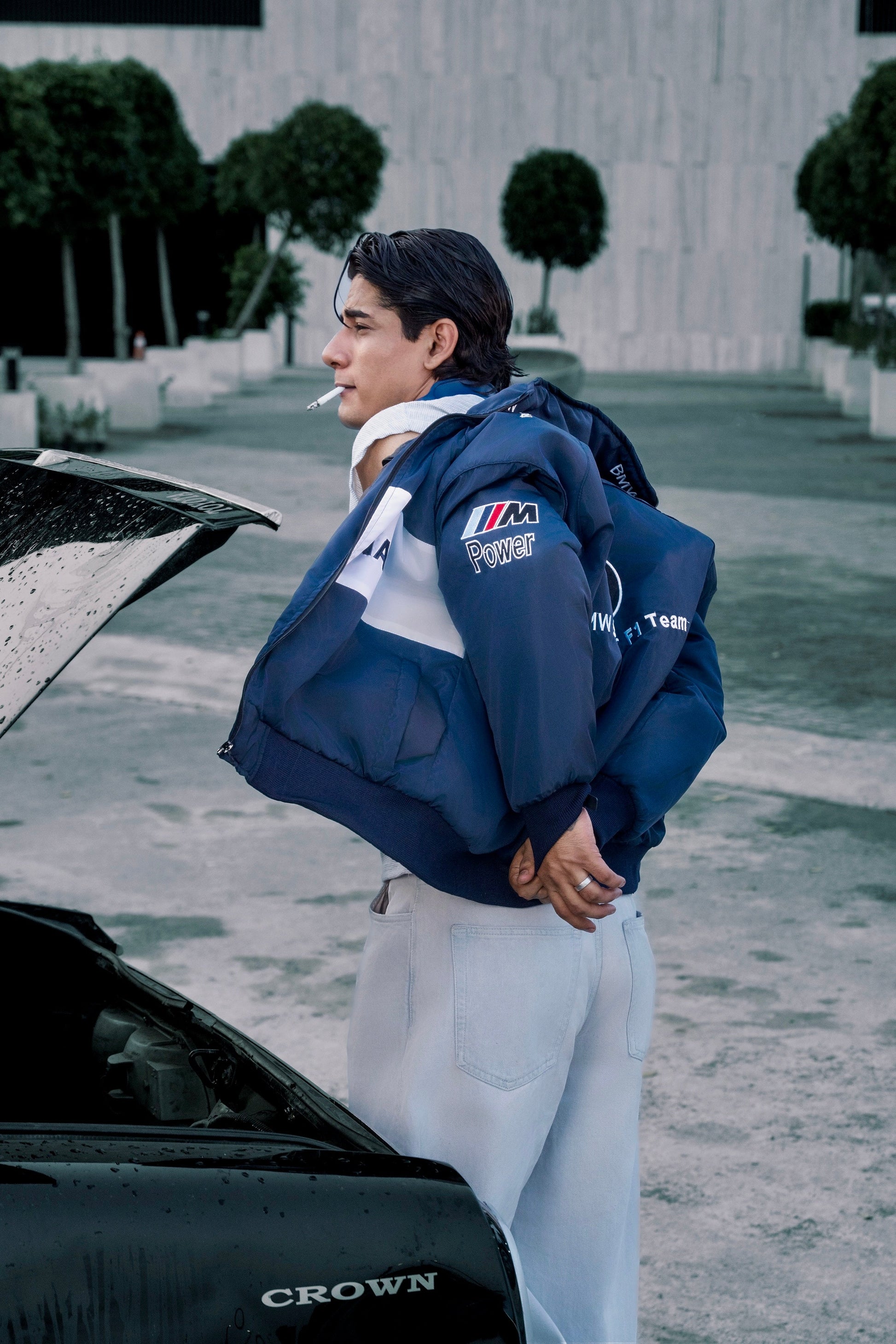 Koti Apparels navy blue BMW racing jacket with embroidered motorsport logos worn by a man standing by a car