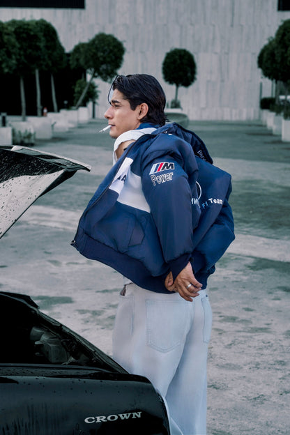 Koti Apparels navy blue BMW racing jacket with embroidered motorsport logos worn by a man standing by a car