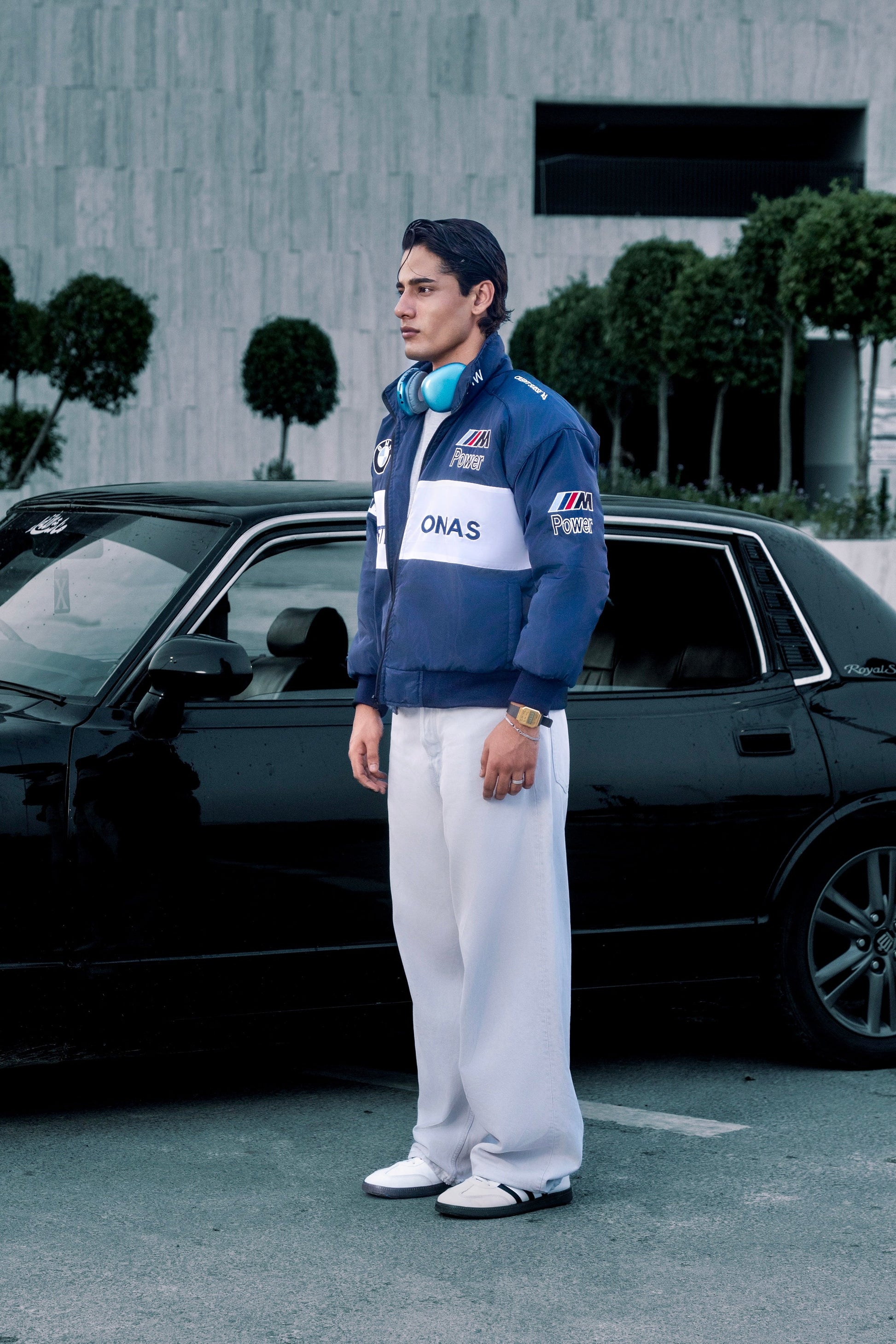 Koti Apparels BMW racing jacket in blue with embroidered motorsport logos worn by a man standing by a black car