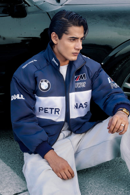 Koti Apparels BMW racing jacket in navy and white with embroidered motorsport logos worn by a man near a black car