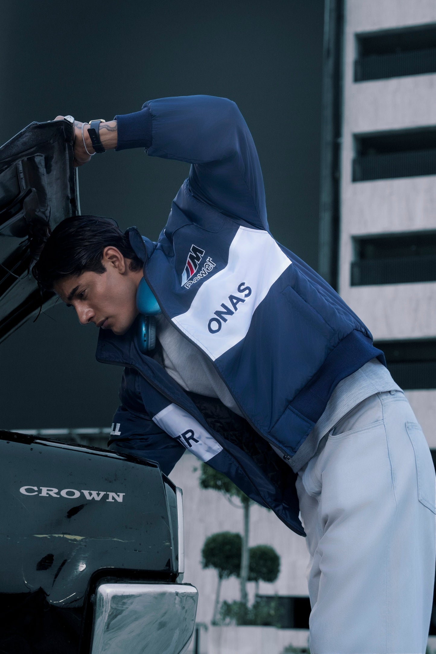 Koti Apparels BMW racing jacket in navy and white with embroidered logos worn by a man checking a car engine