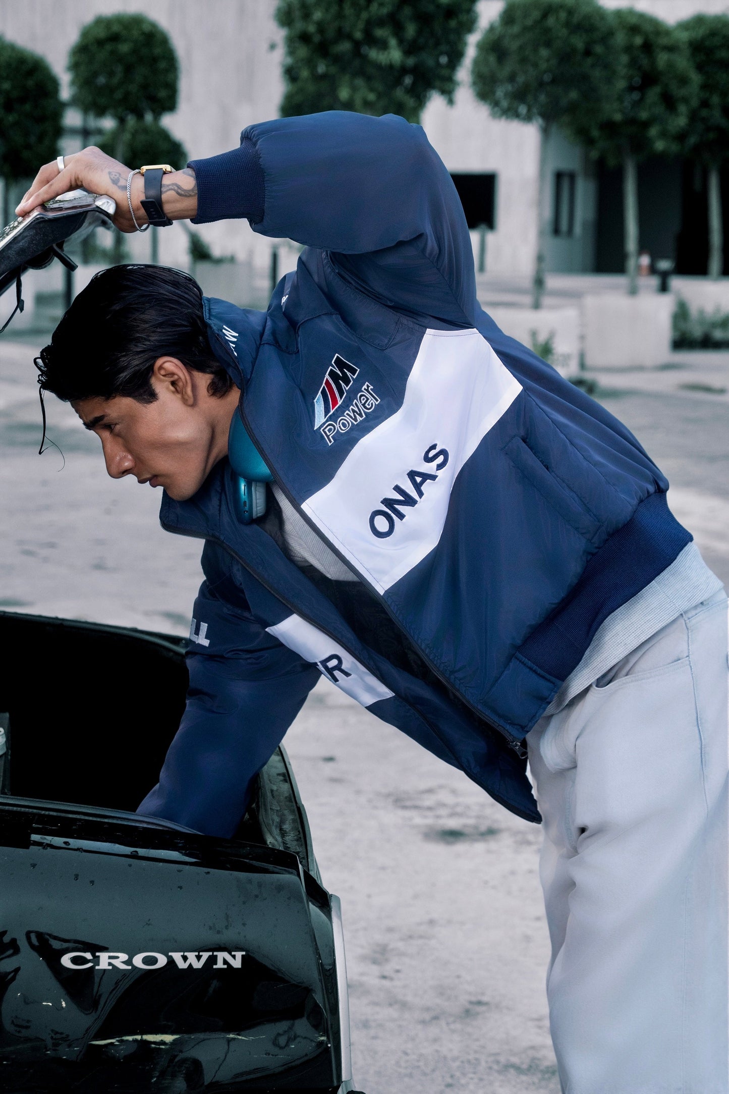 A man wearing a Koti Apparels BMW racing jacket with blue and white panels and embroidered motorsport logos.