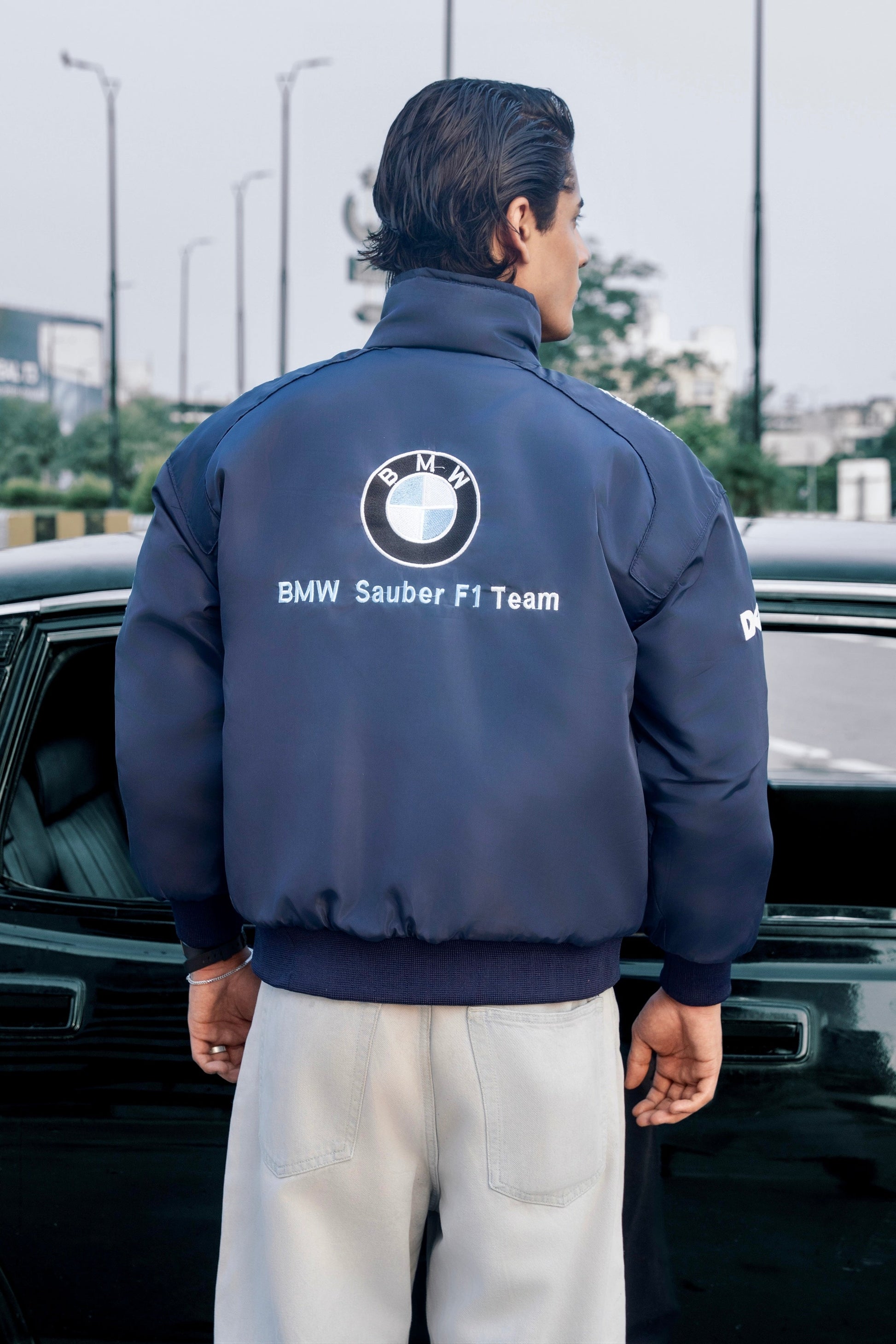 Koti Apparels navy blue BMW Sauber F1 Team racing jacket with embroidered logo worn by a man standing by a car
