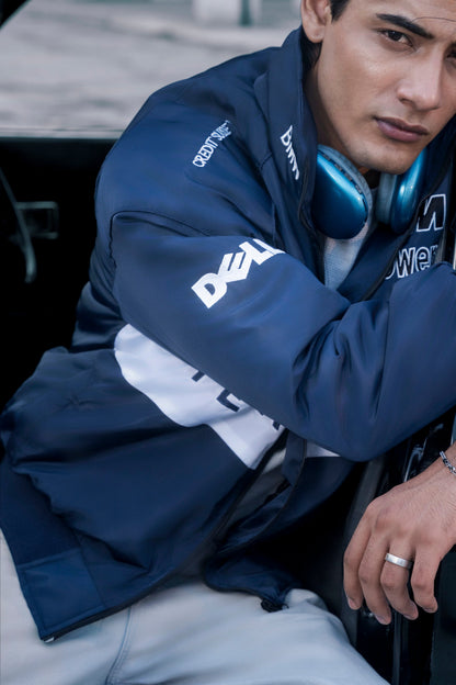 Koti Apparels navy blue BMW racing jacket with white embroidered sponsor logos worn by a man in a car