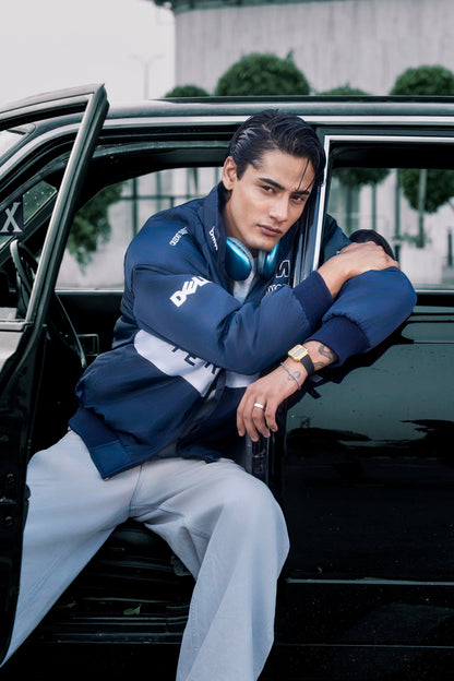 Koti Apparels BMW racing jacket in navy blue with embroidered logos worn by a man leaning against a vintage car
