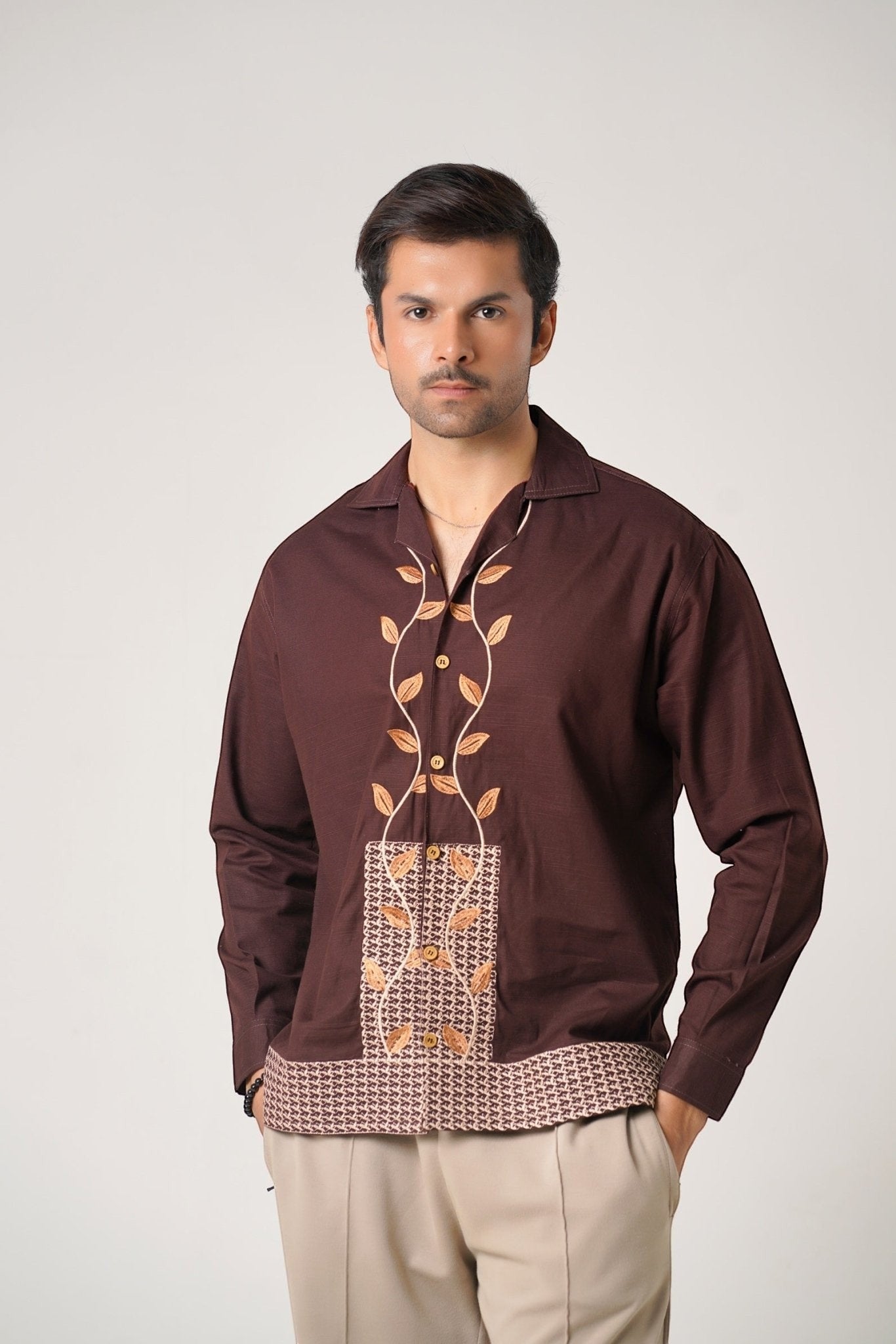 Koti Apparels brown unisex khaddar shirt with leaf embroidery on the front and geometric pattern hem. Open collar, button-down front, full sleeves.