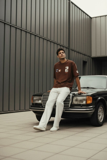 Koti Apparels brown cotton t-shirt with graphic patches and bold numbering, relaxed fit, worn by a man sitting on a vintage car.