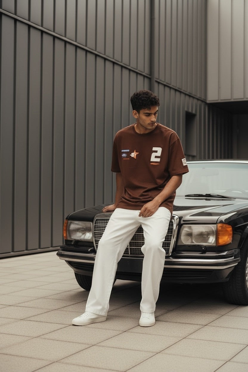 Koti Apparels brown cotton t-shirt with graphic patches and bold number 2, relaxed fit, worn by a man sitting on a car.