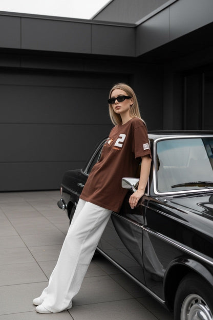 Koti Apparels brown cotton t-shirt with graphic print and bold numbering, worn by a woman leaning on a vintage car.