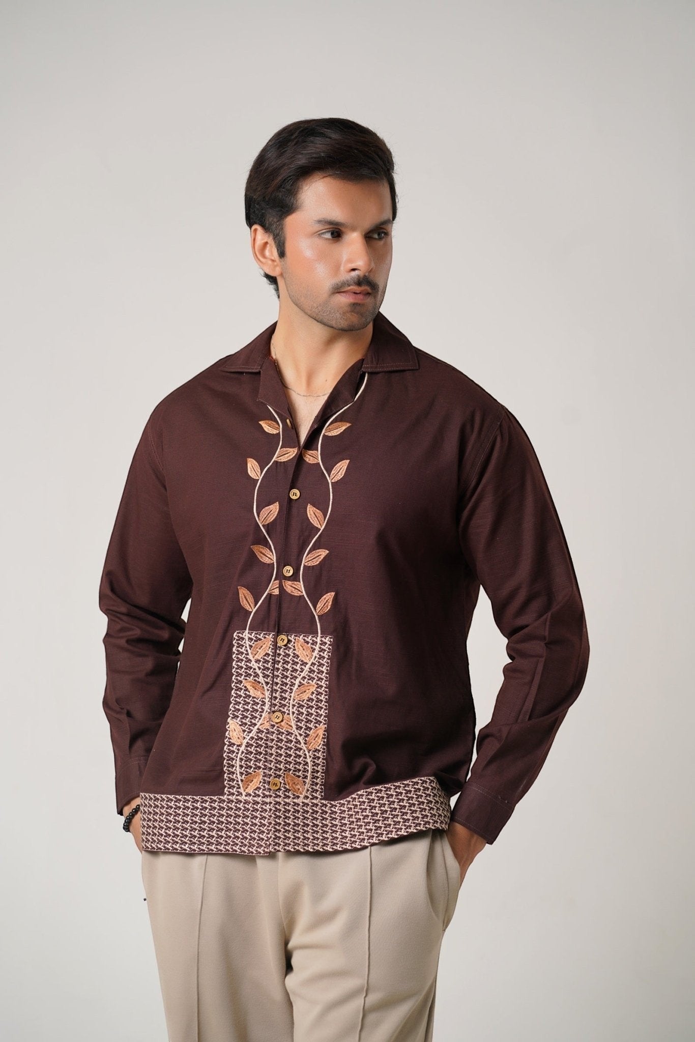 Koti Apparels unisex brown khaddar shirt with leaf embroidery on the placket and geometric pattern hem. Open collar, button-down front, full sleeves.