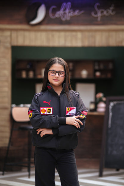 A young girl wearing a black Koti Apparels Ferrari racing jacket with red and white sponsor logos and Puma branding.