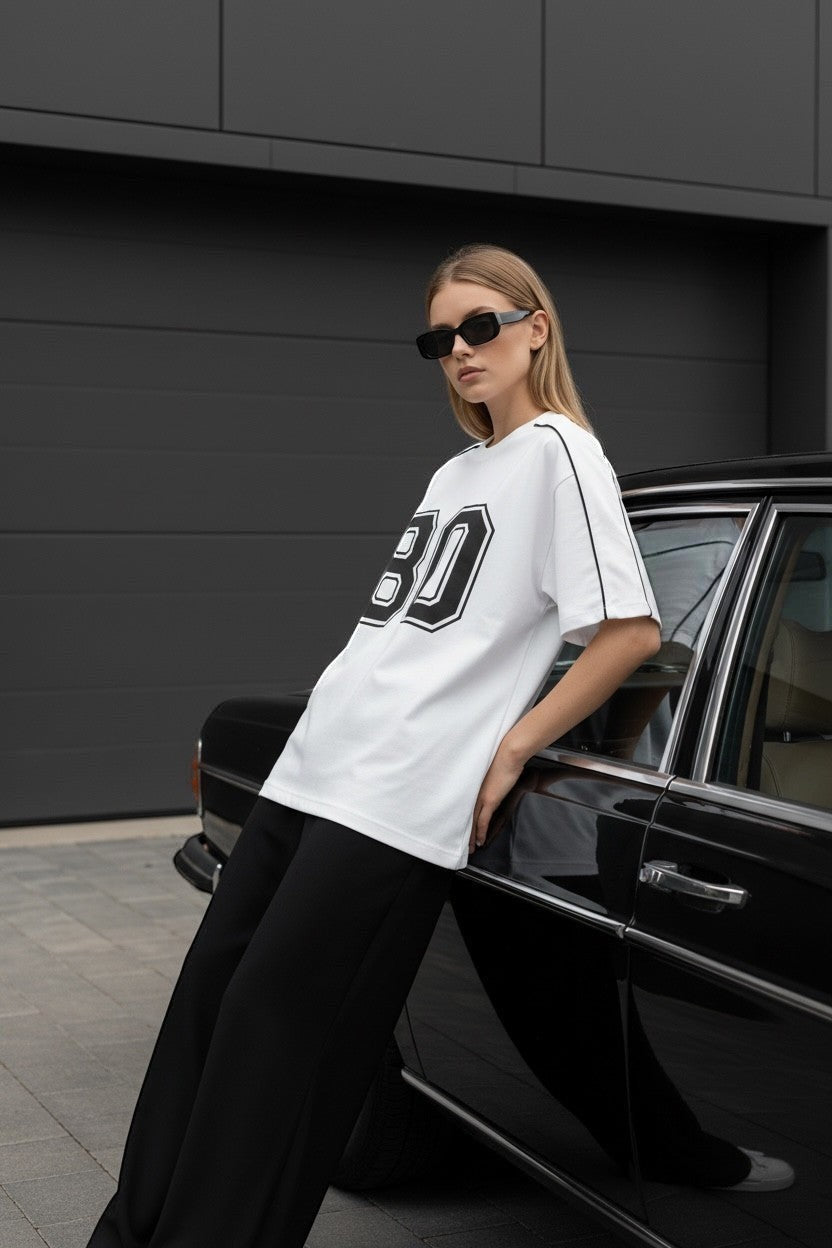 Koti Apparels white cotton blend t-shirt with black "80" graphic and piping. Model leans on a vintage car.