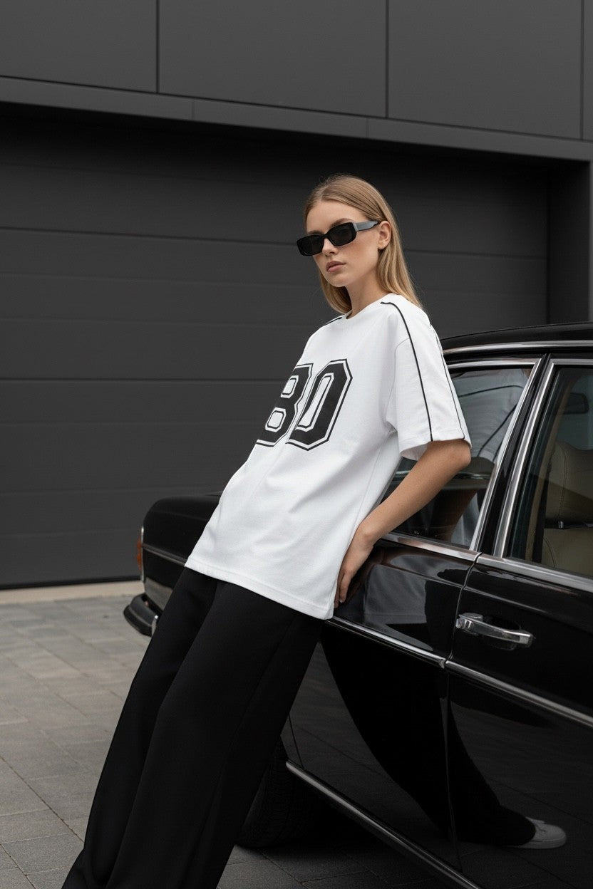 Koti Apparels white cotton blend t-shirt with black "80" graphic and piping. Model leans on a vintage car.