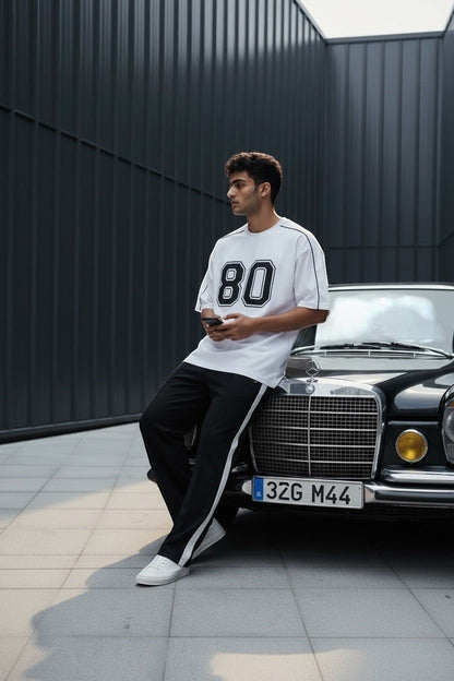 Koti Apparels white cotton blend t-shirt with black "80" graphic and piping. Model leans on a vintage car.
