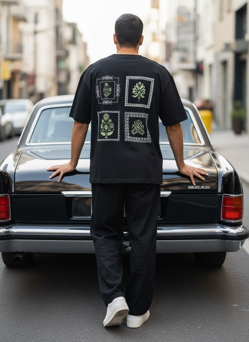 Koti Apparels black cotton blend t-shirt with graphic print on back featuring botanical squares and paisley motifs in muted green and white.