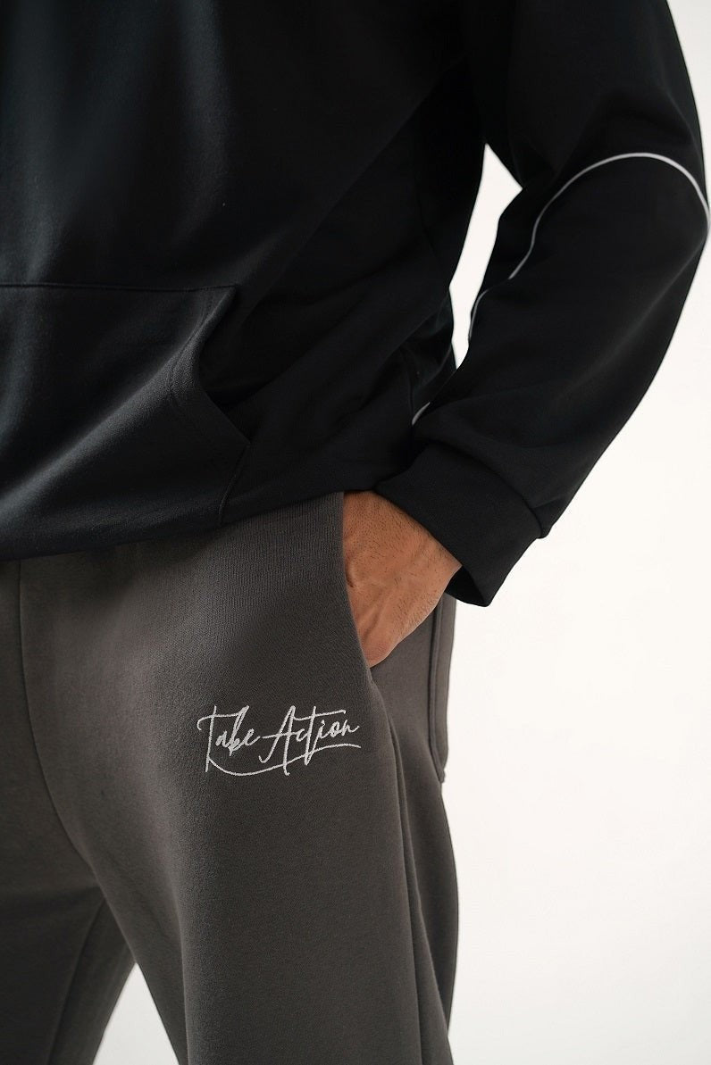 Koti Apparels heavyweight unisex black hoodie with white piping and charcoal grey sweatpants with embroidered "Take Action" logo.