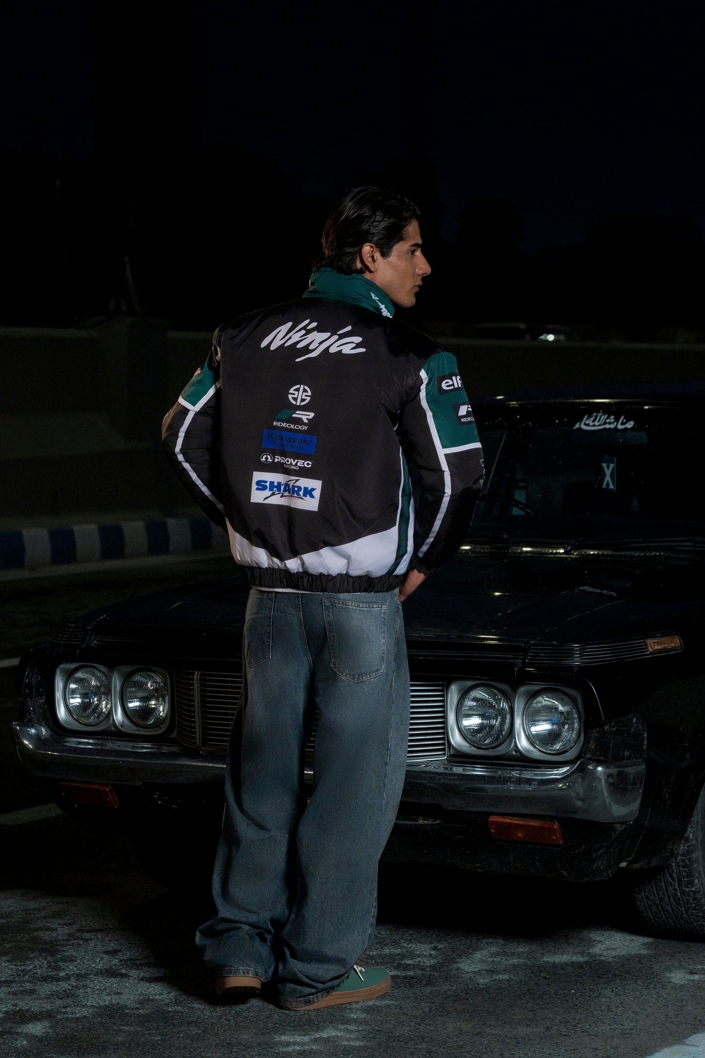 Koti Apparels Kawasaki racing jacket in black and green with Ninja branding, worn by a man leaning on a vintage car.