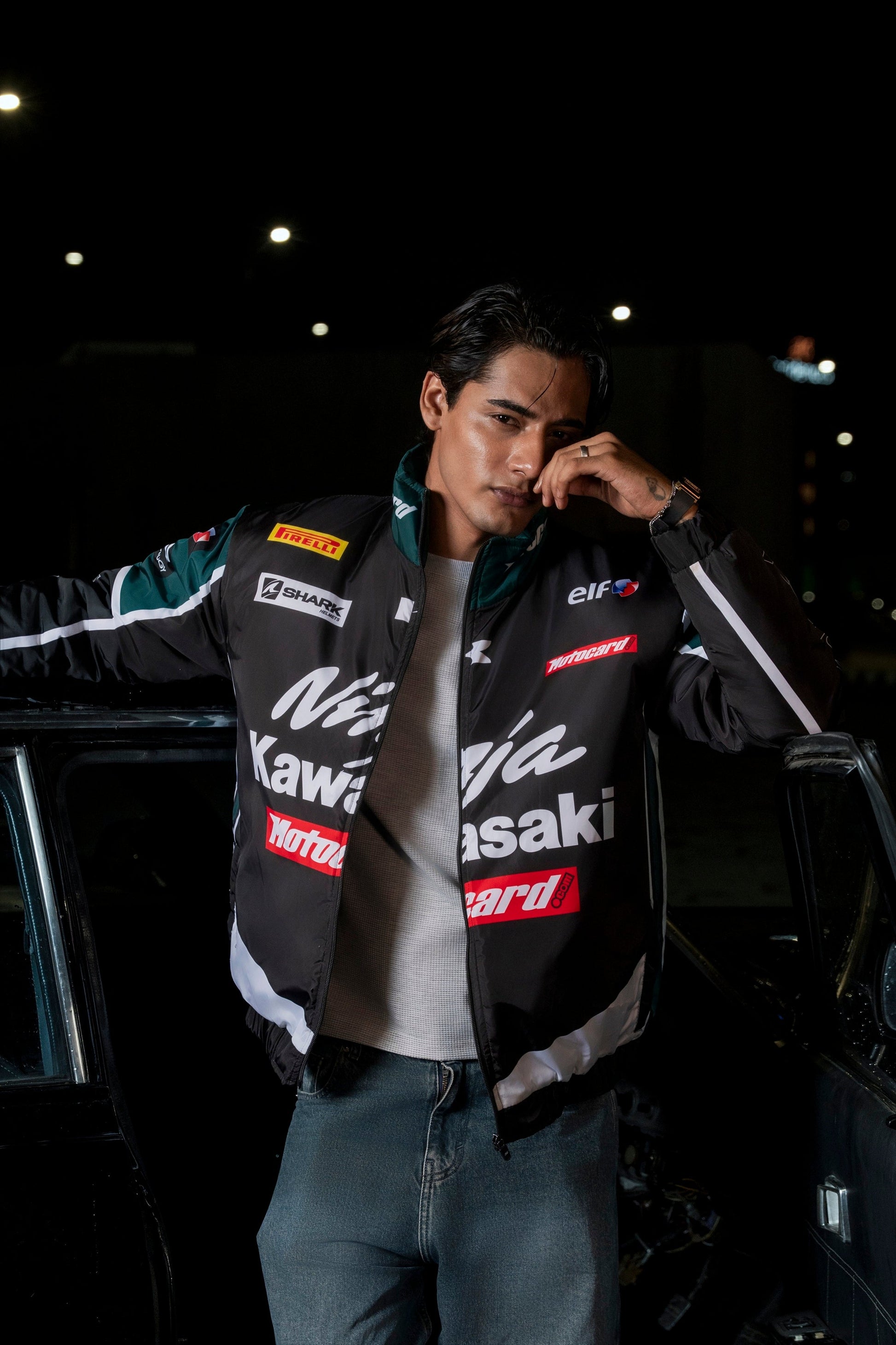 Man wearing a Koti Apparels Kawasaki racing jacket in black and green with sponsor logos at night