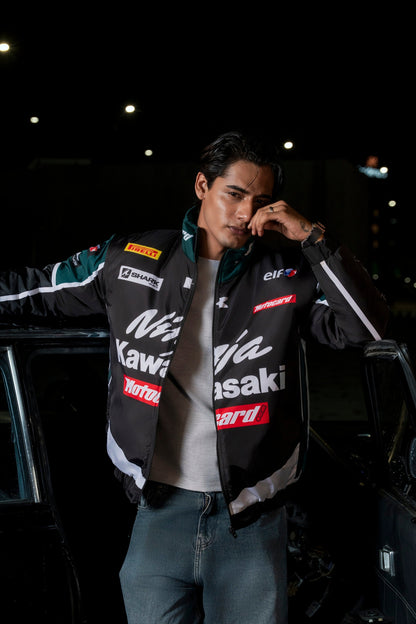 Man wearing a Koti Apparels Kawasaki racing jacket in black and green with sponsor logos at night