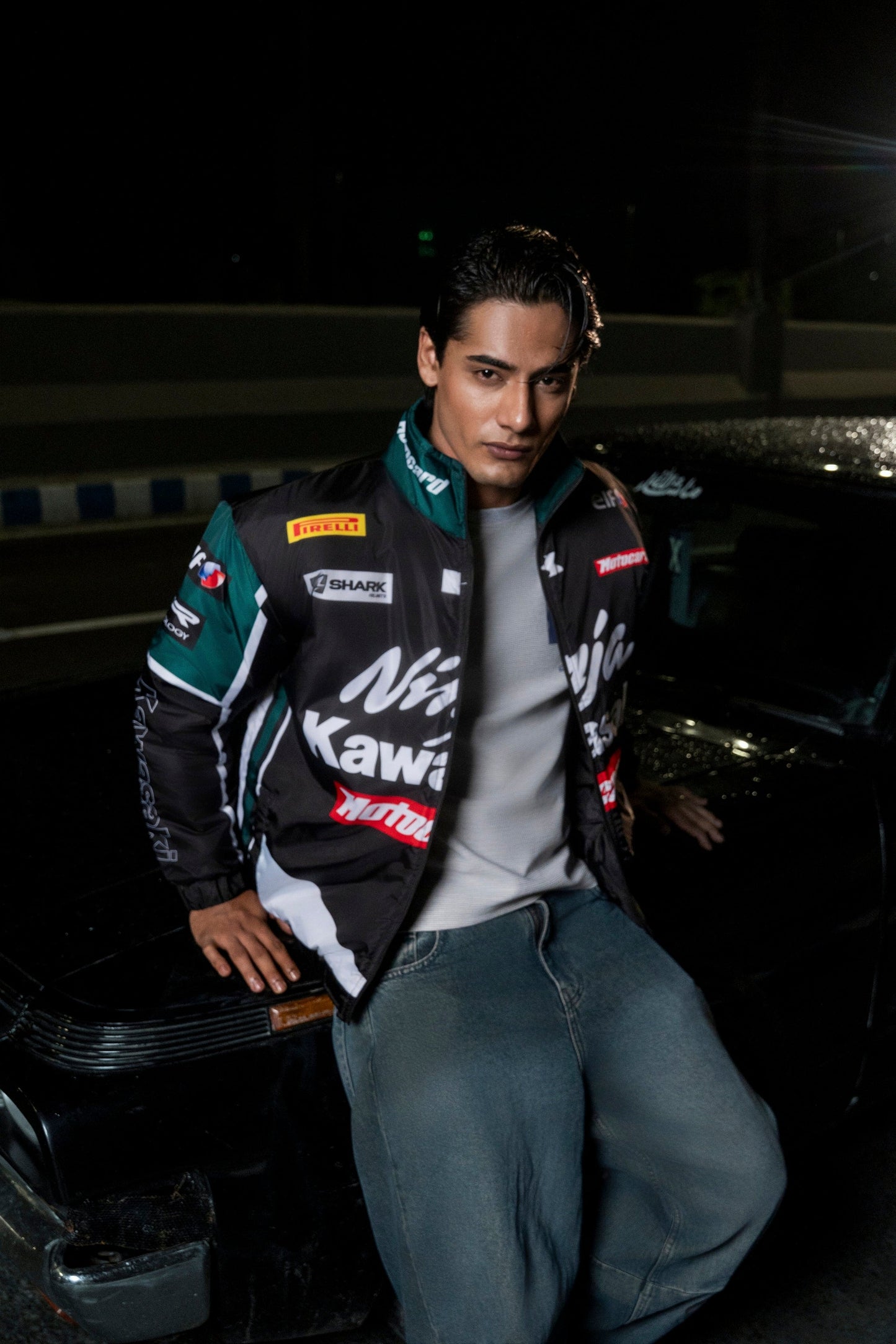 Koti Apparels Kawasaki racing jacket in black and green polyester worn by a man leaning against a car at night