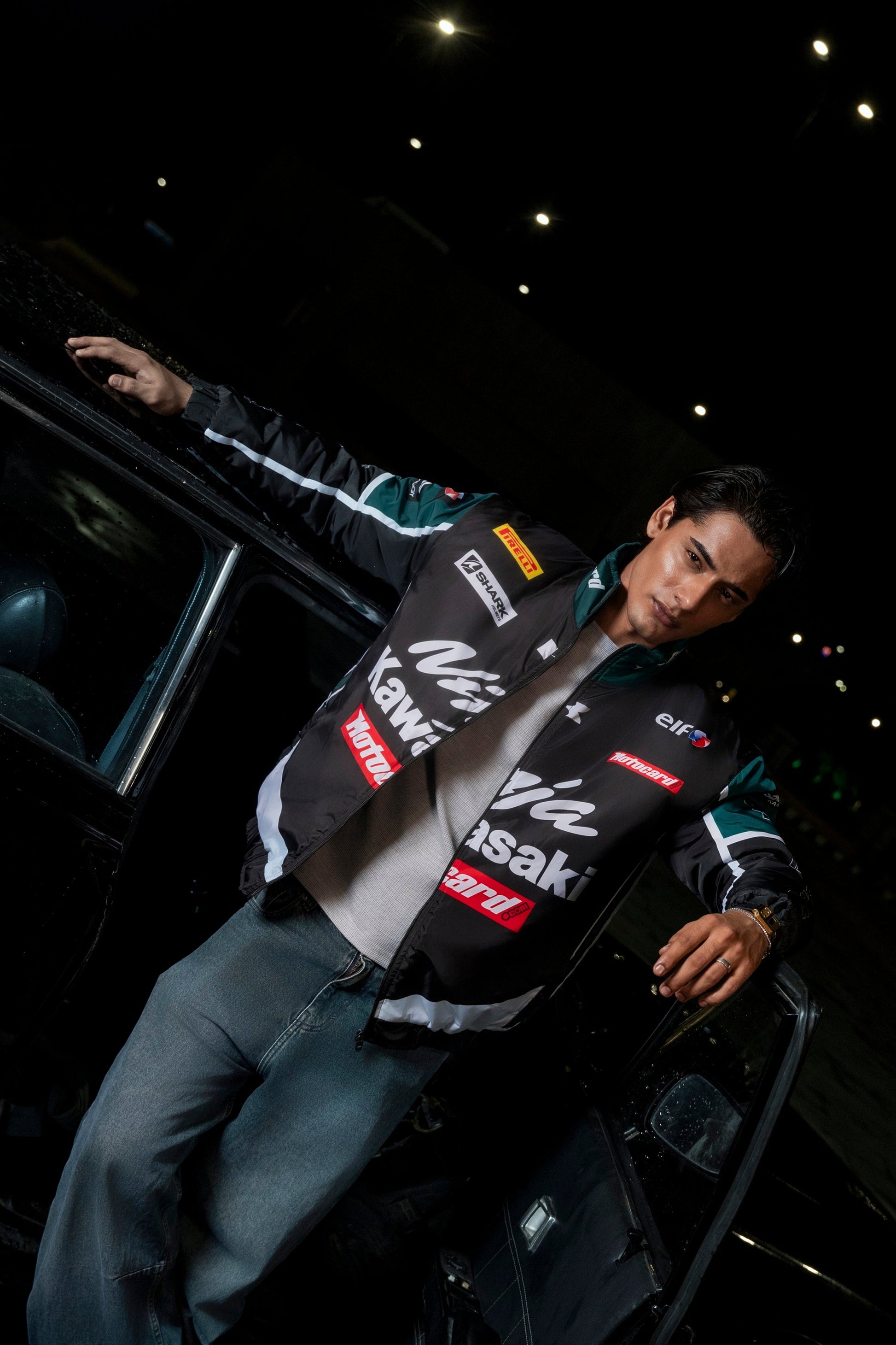 Koti Apparels Kawasaki racing jacket in black and green polyester worn by a man leaning against a car at night