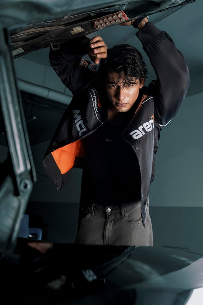 Koti Apparels McLaren F1 racing jacket with orange lining and detailed embroidery, worn by a man in a garage setting.
