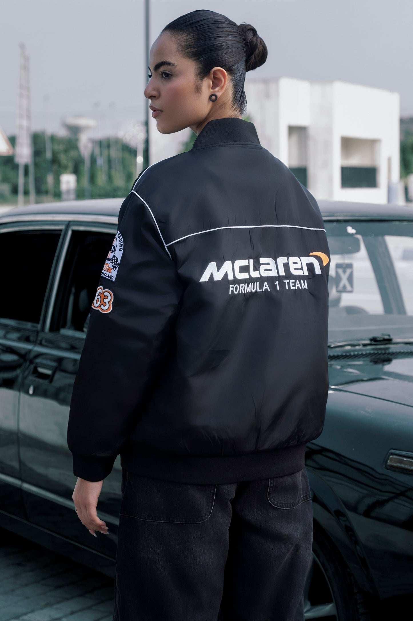 Model wearing a black Koti Apparels McLaren F1 racing jacket with premium embroidered logos and quilted lining.